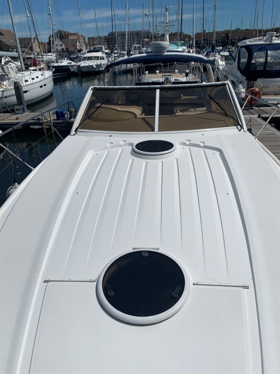 A view from above a white boat's deck, featuring portholes, with multiple boats docked at a marina in the background.